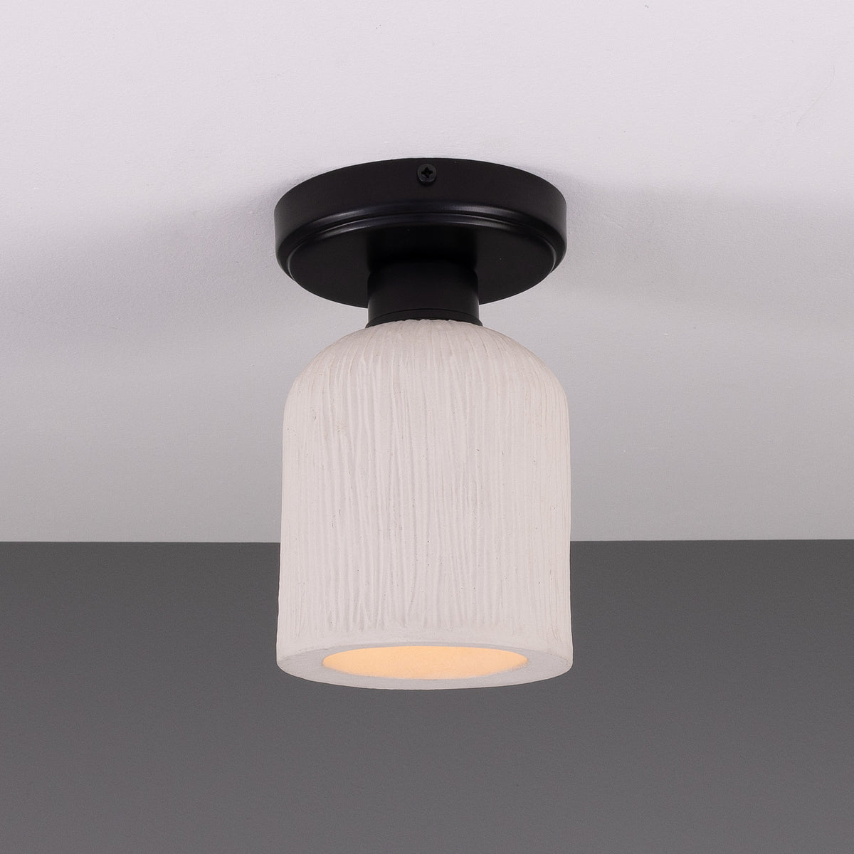 Osier Ceramic Flush Ceiling Light with a matt white striped textured shade and round black ceiling plate, shown glowing against a plain grey background.