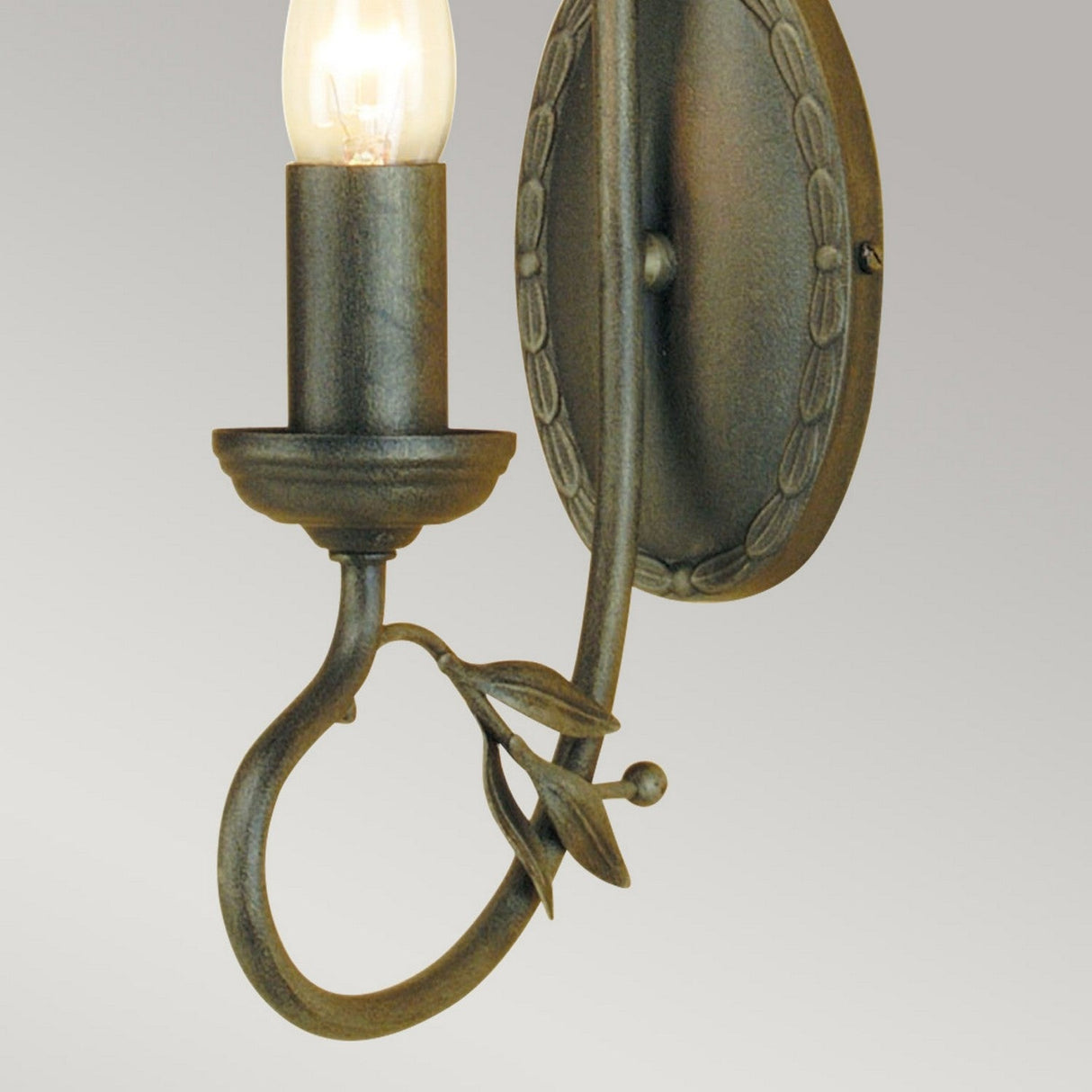 Introducing the Olivia 1 Light Wall Light in Black/Gold Patina, a handmade decorative fixture featuring a candlestick-style bulb. Its metal frame is adorned with an intricate leaf motif and boasts a stunning black/gold patina finish. Set against a plain gray background, this elegant wall light adds a touch of classic charm.