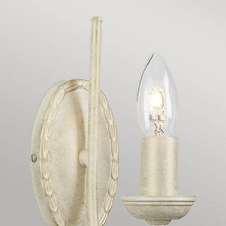 The Olivia 1 Light Wall Light in Ivory/Gold Patina is a vintage-style wall sconce with an oval backplate and a single candle-shaped bulb. This handmade piece showcases an off-white finish complemented by an elegant decorative edge design.