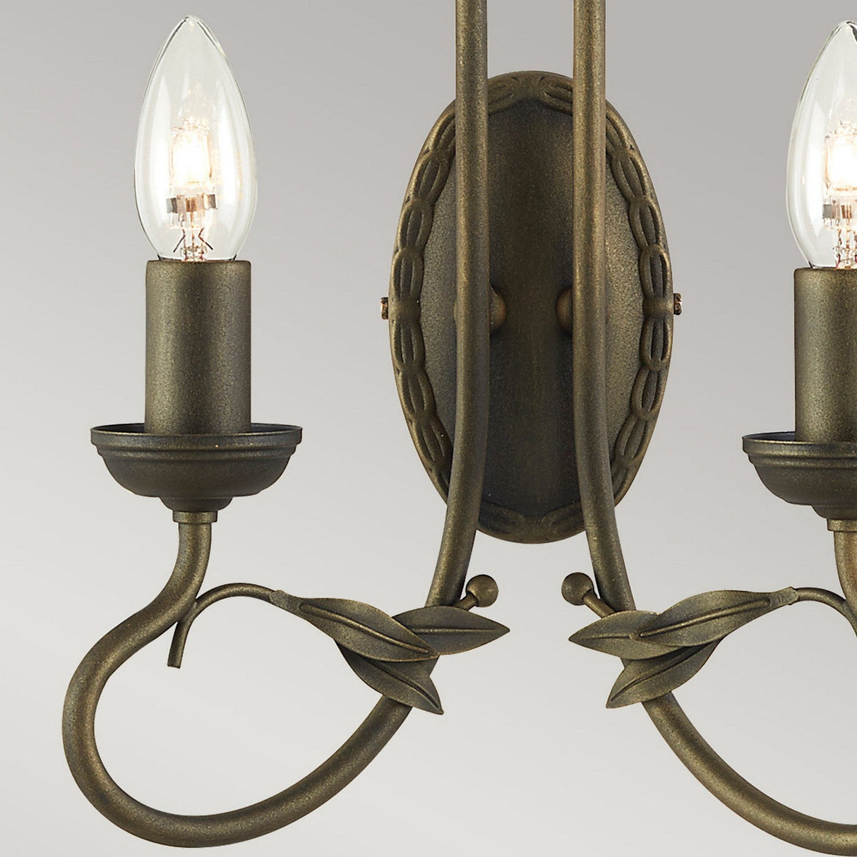 A detailed view of the Olivia 2 Light Wall Light - Black/Gold Patina, featuring a vintage design with two elegantly curved metal arms. The arms display a black and gold patina finish, each holding a candle-shaped bulb. Leaf-like decorations accentuate its handcrafted lighting design against a neutral gray backdrop.