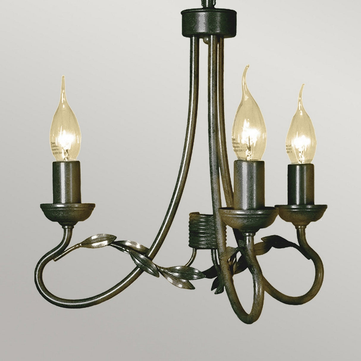 The Olivia 3 Light Chandelier showcases an artisanal wrought iron design with a candle-style aesthetic, featuring three upward-facing lights that resemble candle flames. Each light is supported by elegantly curved metal arms embellished with leaf accents, all finished in a striking black/gold patina against a neutral backdrop.