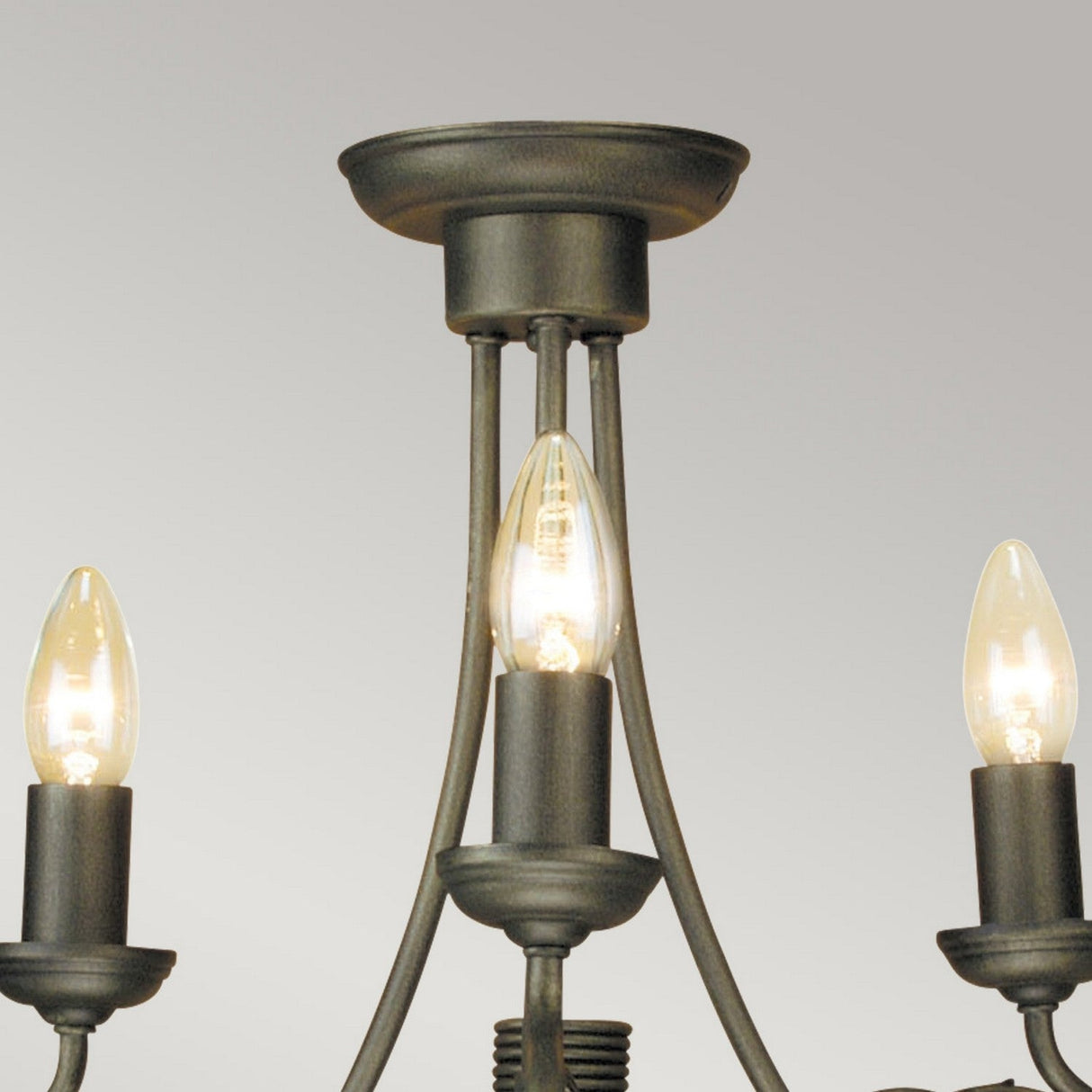 Close-up of the Olivia 3 Light Chandelier - Black/Gold Patina, showcasing its traditional craftsmanship. It includes three candle-style bulbs nestled in a black metal frame adorned with a subtle gold patina, all elegantly mounted on a circular base against a simple gray backdrop.