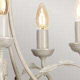 A close-up view of the Olivia 5 Light Chandelier - Ivory/Gold Patina highlights a candle-shaped bulb nestled in a matte silver holder. Its graceful leaf-like accents perfectly enhance transitional interiors, and the simple light gray background underscores its timeless appeal.