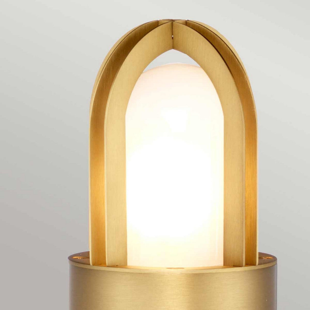 The Paignton 1 Light Bollard - Brushed Brass is a modern lighting fixture that features a warm, glowing bulb encased in an elegant, arched frame. Its solid brass construction seamlessly blends contemporary and classic elements with its circular base and sleek, smooth metal finish.