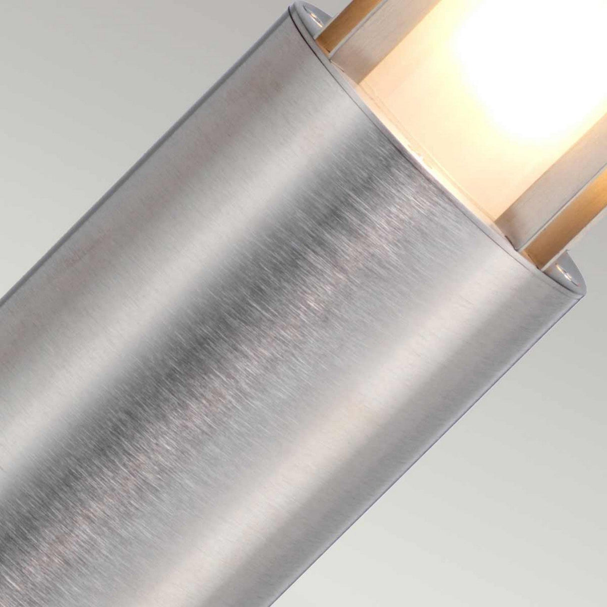 A close-up of the Paignton 1 Light Bollard in stainless steel showcases its sleek, cylindrical shape with a brushed texture and frosted glass that emits a warm glow. Its minimalist design, resembling a vertical bollard, adds a modern aesthetic against a neutral backdrop—ideal for enhancing elegance in outdoor lighting.