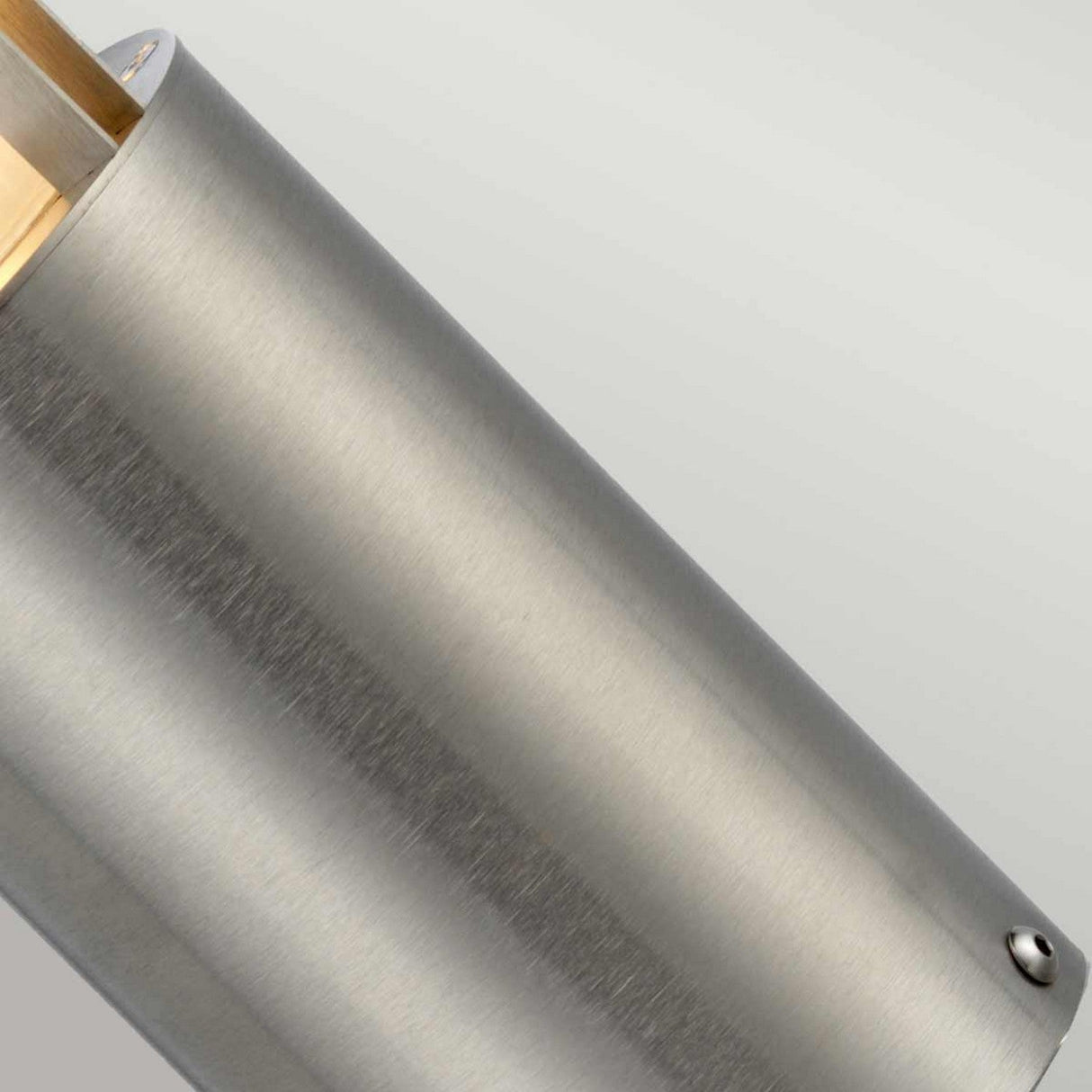 Close-up of the Paignton 1 Light Mini Bollard in brushed stainless steel, showcasing its smooth, matte finish. A small, round screw embellishes the top edge. The lighting accentuates the texture and sheen of its metal surface against a neutral background, making it ideal for outdoor lighting applications.