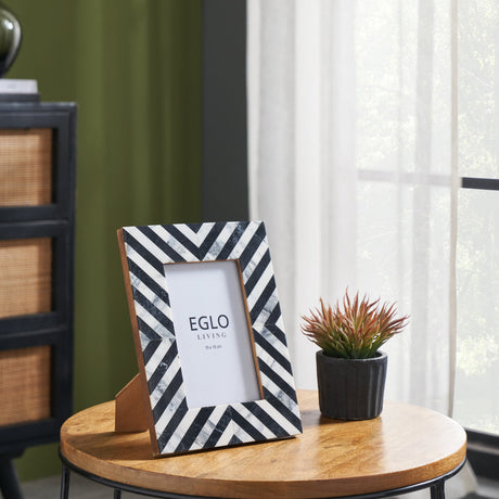 Panaon Photo Frame with black and white marbled chevron border and glass front, displayed on a wooden table beside a small potted plant.