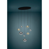 Pantoja 8-light cluster pendant with ribbed amber and smoke glass globes at staggered heights, suspended from a black oval ceiling canopy against a dark teal backdrop.