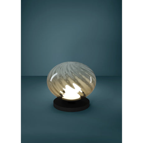 Pantoja LED table lamp with a flattened, ribbed amber glass globe illuminated on a round black steel base, set against a dark teal background.