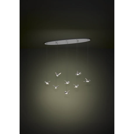 Paratebueno 8-light linear pendant light in chrome, with eight bird-shaped LED shades in steel and plastic hanging at staggered heights from an oval ceiling canopy, against a dark background.