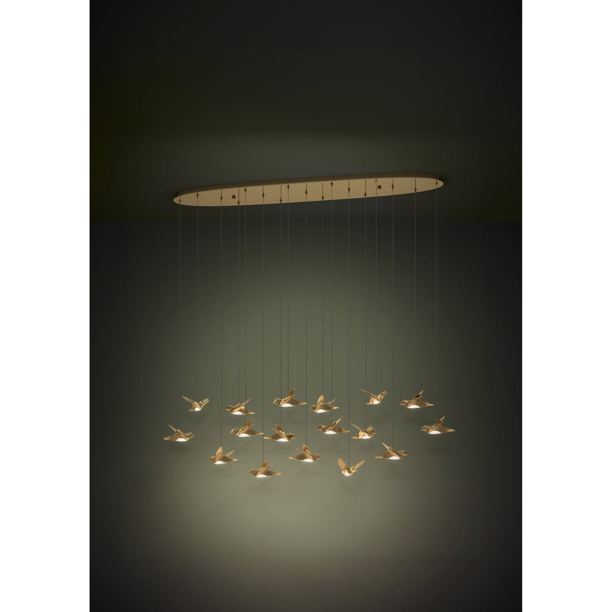 Paratebueno 2 linear pendant light with an oval brass canopy and seventeen bird-shaped shades at varying heights, illuminated with warm white LED light against a dark background.
