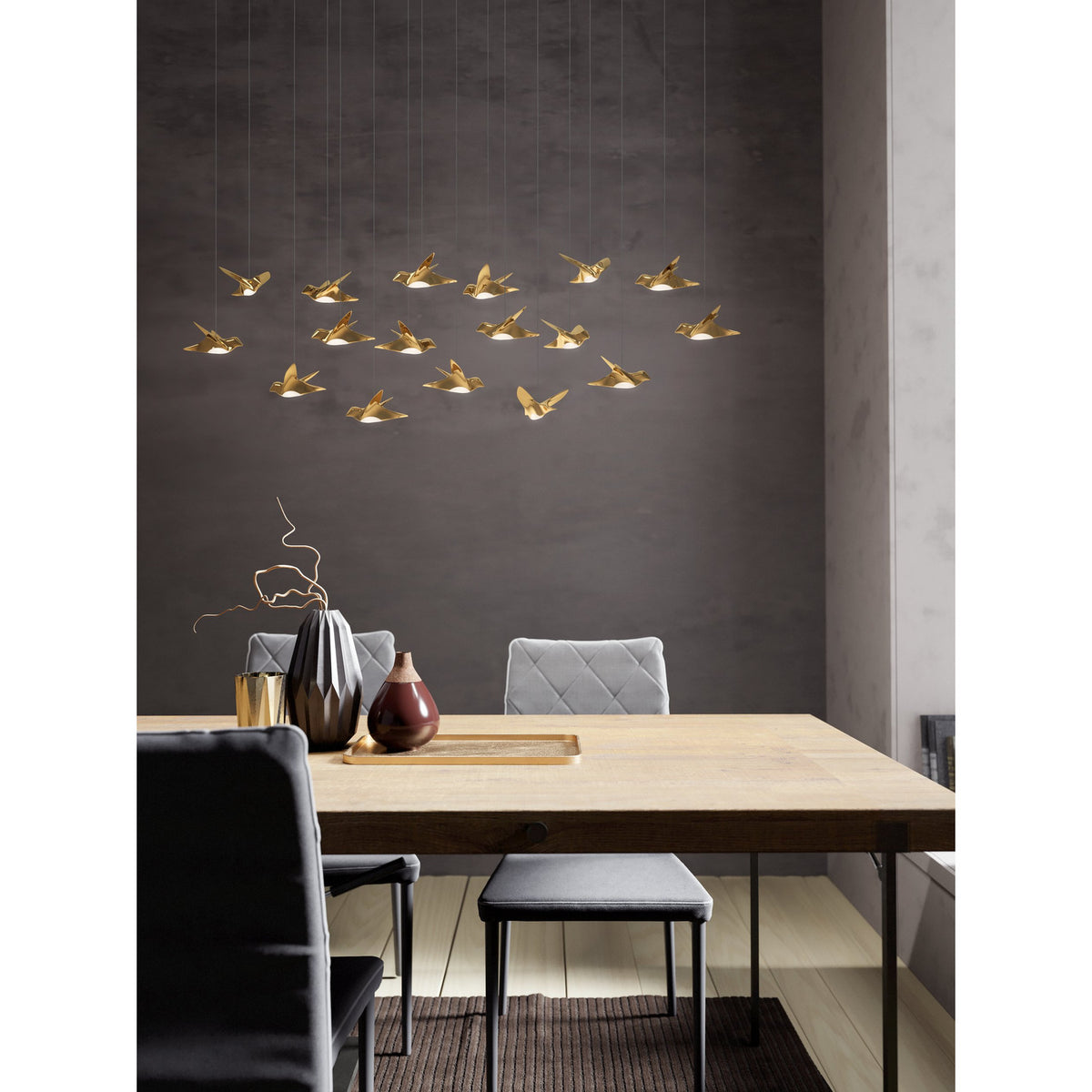 Paratebueno 2 17 Light Linear Pendant Light in brass, bird-shaped shades at varied heights, hung above a dining table in a grey-walled dining room.