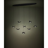 Paratebueno 8 Light Linear Pendant in black, oval ceiling plate with eight cords suspending bird-shaped LED shades at varying heights, shown glowing warm white in a dim room.