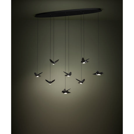 Paratebueno 8 Light Linear Pendant in black, oval ceiling plate with eight cords suspending bird-shaped LED shades at varying heights, shown glowing warm white in a dim room.