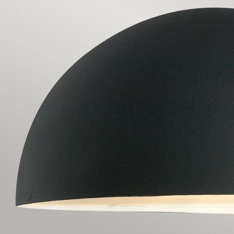 Close-up of a contemporary half-sphere wall lantern with a smooth black finish against a light gray background. The interior is white, casting a warm glow.