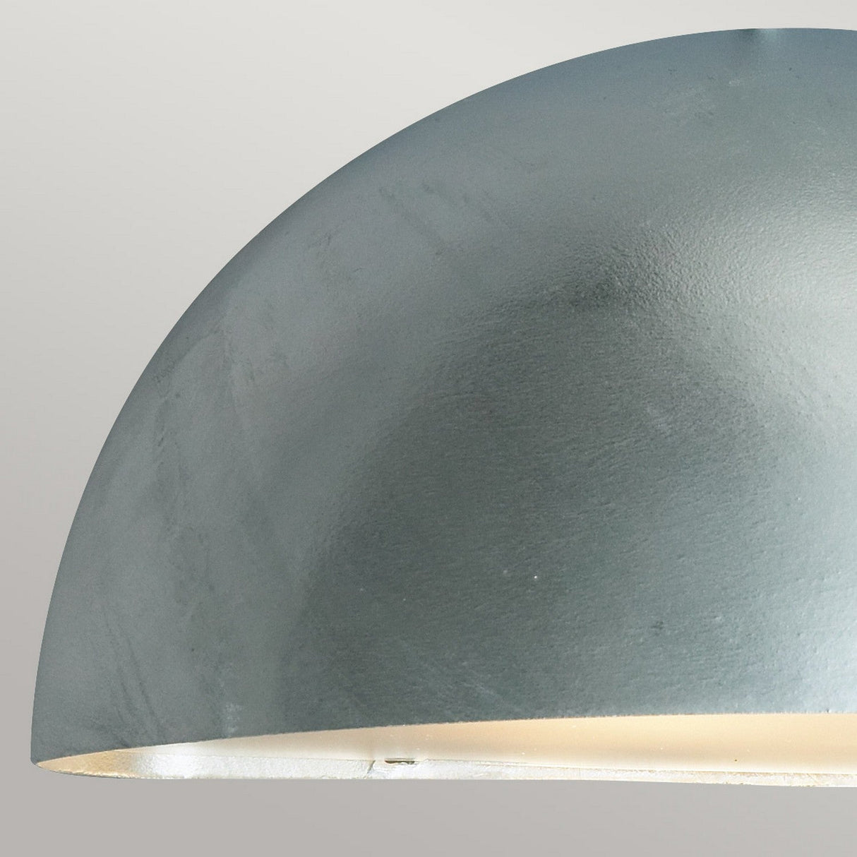 Close-up of the Paris Outdoor Small 1 Light Wall Lantern in silver, featuring a gray, dome-shaped design crafted from galvanized steel with a smooth, matte finish. Designed for outdoor lighting with an IP43 rating, its interior emits a soft, warm glow against a pale background.