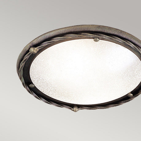 The Pembroke 1 Light Flush Light in black/gold is a round, ornate fixture with a frosted glass cover and a decorative hand-forged iron rim adorned with a twisted pattern and small metal accents. It is set against a plain light gray background.
