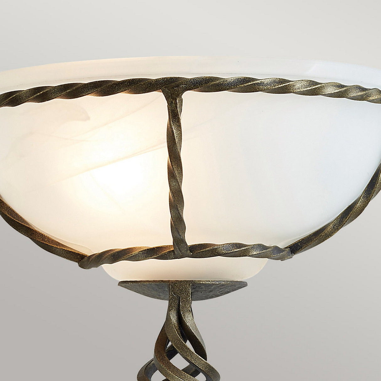 Close-up of the elegant Pembroke Wall Light - Black/Gold showcasing a frosted glass bowl shade. It features a twisted, hand-forged iron frame in a dark metallic finish, adding a sophisticated, vintage touch. The light emits a soft, warm glow against a neutral background.