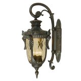 The Philadelphia 3 Light Outdoor Large Down Wall Light in Old Bronze showcases vintage-style charm with its ornate metal detailing and curved arm. With amber glass panels, it is designed to accommodate a candle or light bulb.