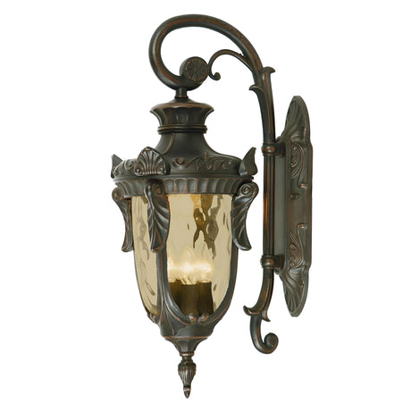 The Philadelphia 3 Light Outdoor Large Down Wall Light in Old Bronze showcases vintage-style charm with its ornate metal detailing and curved arm. With amber glass panels, it is designed to accommodate a candle or light bulb.