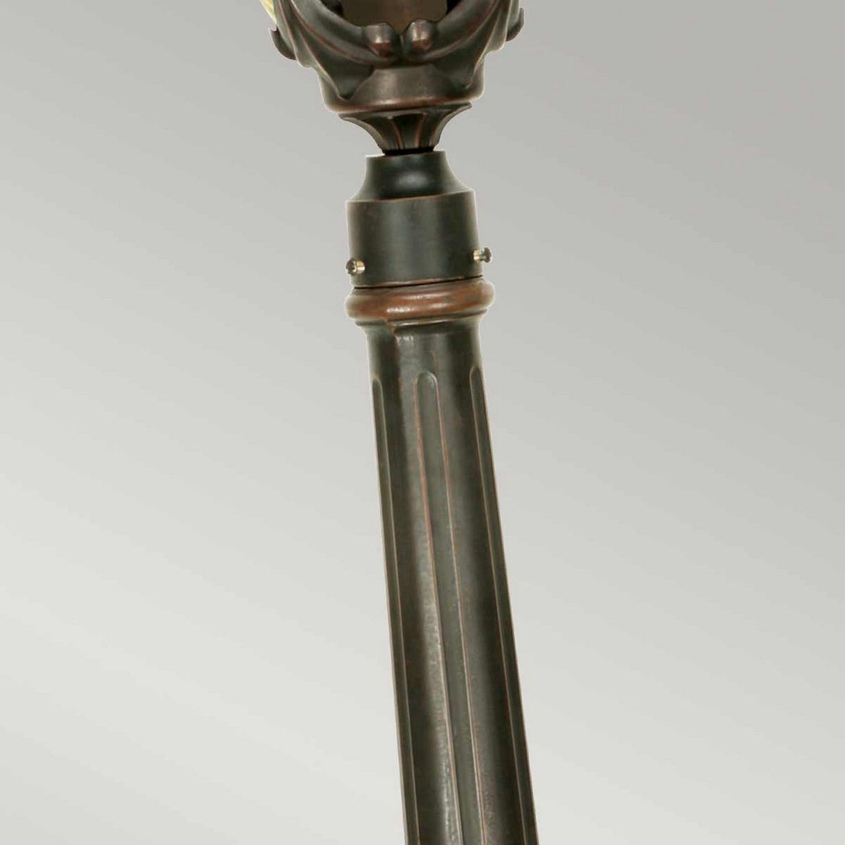 Close-up of a tall, ornate metal stand featuring intricate detailing near the top and a ribbed design on the shaft. The Philadelphia 1 Light Medium Pillar - Old Bronze showcases a dark, polished finish. Ideal for outdoor lighting, it stands elegantly against the plain light gray background.