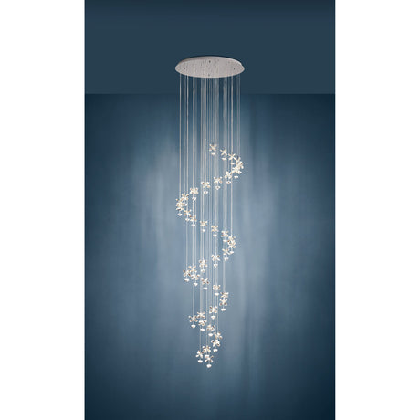 Pianopoli 1 pendant light with 40 clear glass flower-shaped drops cascading in a spiral from a round chrome ceiling plate, shown against a dark teal wall.