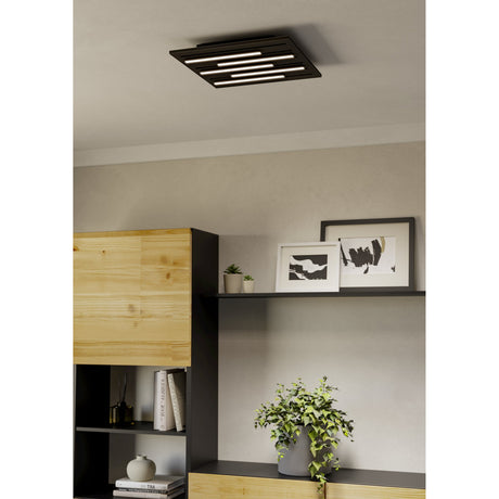 Pitrignani Smart LED Flush Ceiling Light, square matt black panel with staggered illuminated strips, mounted flush on a living room ceiling above a wooden and black shelving unit.