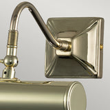 A close-up of the Picture Light 1 Light Small in polished brass showcases its shiny, rectangular base and elegantly curved arm. The metallic surface beautifully reflects light, highlighting its smooth and polished finish against a plain gray background, making it perfect for illuminating artwork.