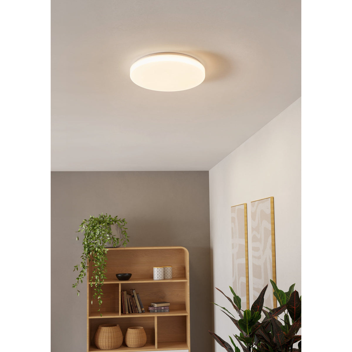 Pogliola-E round LED flush ceiling light in white, 31cm disc shade on a grey ceiling, shown lit in a hallway setting with wooden shelving and plants below.