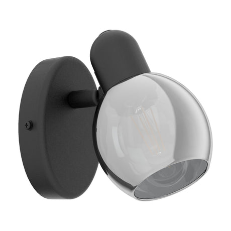 Pollica wall spotlight in black with a round steel wall plate, short angled arm, and smoke-tinted glass globe shade, shown on a plain white background.