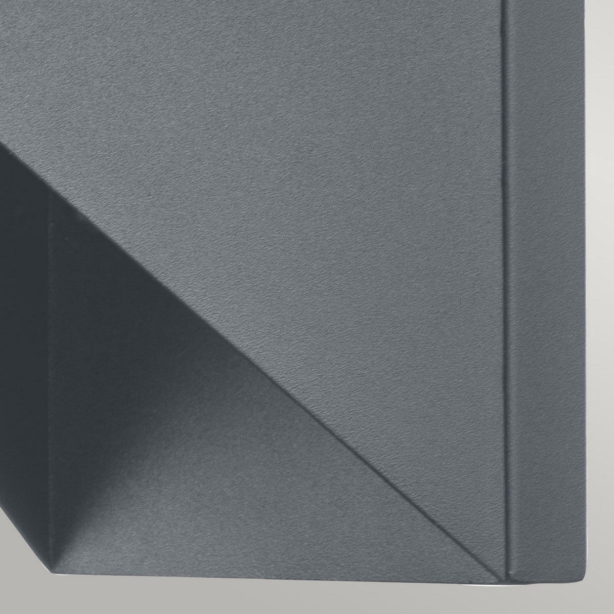 A close-up of the Portfino 1 Light Outdoor Wall Light in grey showcases its geometric shape with sharp lines and angles, casting a shadow on a flat surface. Its design mirrors nautical lighting, providing an IP44 rated aesthetic that results in a visually appealing abstract pattern.