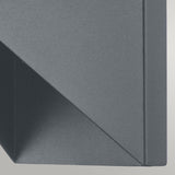 A close-up of the Portfino 1 Light Outdoor Wall Light in grey showcases its geometric shape with sharp lines and angles, casting a shadow on a flat surface. Its design mirrors nautical lighting, providing an IP44 rated aesthetic that results in a visually appealing abstract pattern.