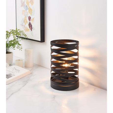 Pranvorne Table Lamp in black steel with crisscrossing bands forming a cylindrical shade, lit and displayed on a marble console beside a plant and artwork.