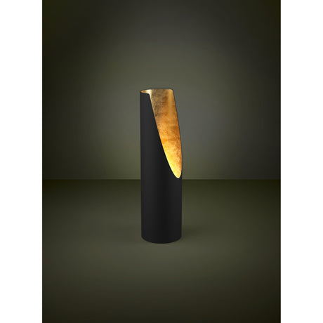 Prebone Table Lamp in black steel with a slim cylindrical body, angled cut revealing a gold leaf-textured inner face, shown lit against a dark background.