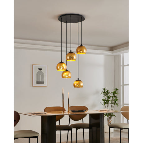 Prelvelle Glass 5 Light Pendant in black, featuring five staggered crackled-gold glass bowl shades on black steel cords from a round black ceiling canopy, shown above a dining table.