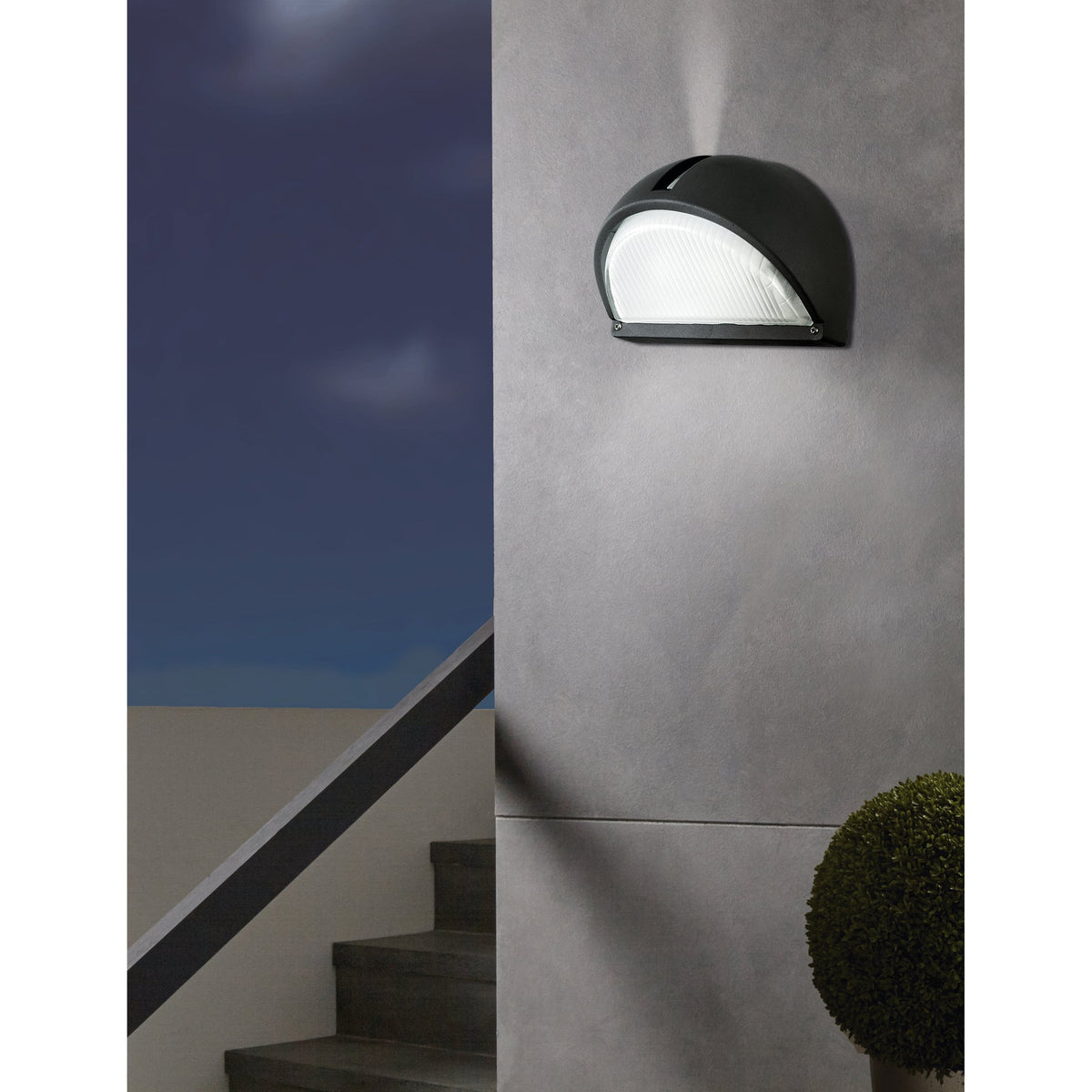 Prinorne Outdoor Wall Light in black cast aluminium with a ribbed glass shade, mounted on a grey exterior wall near a staircase at night.