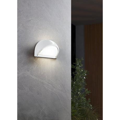 Prinorne Outdoor Wall Light in white, a half-dome aluminium fixture with ribbed glass shade, shown illuminated on a grey stone wall near an entrance.