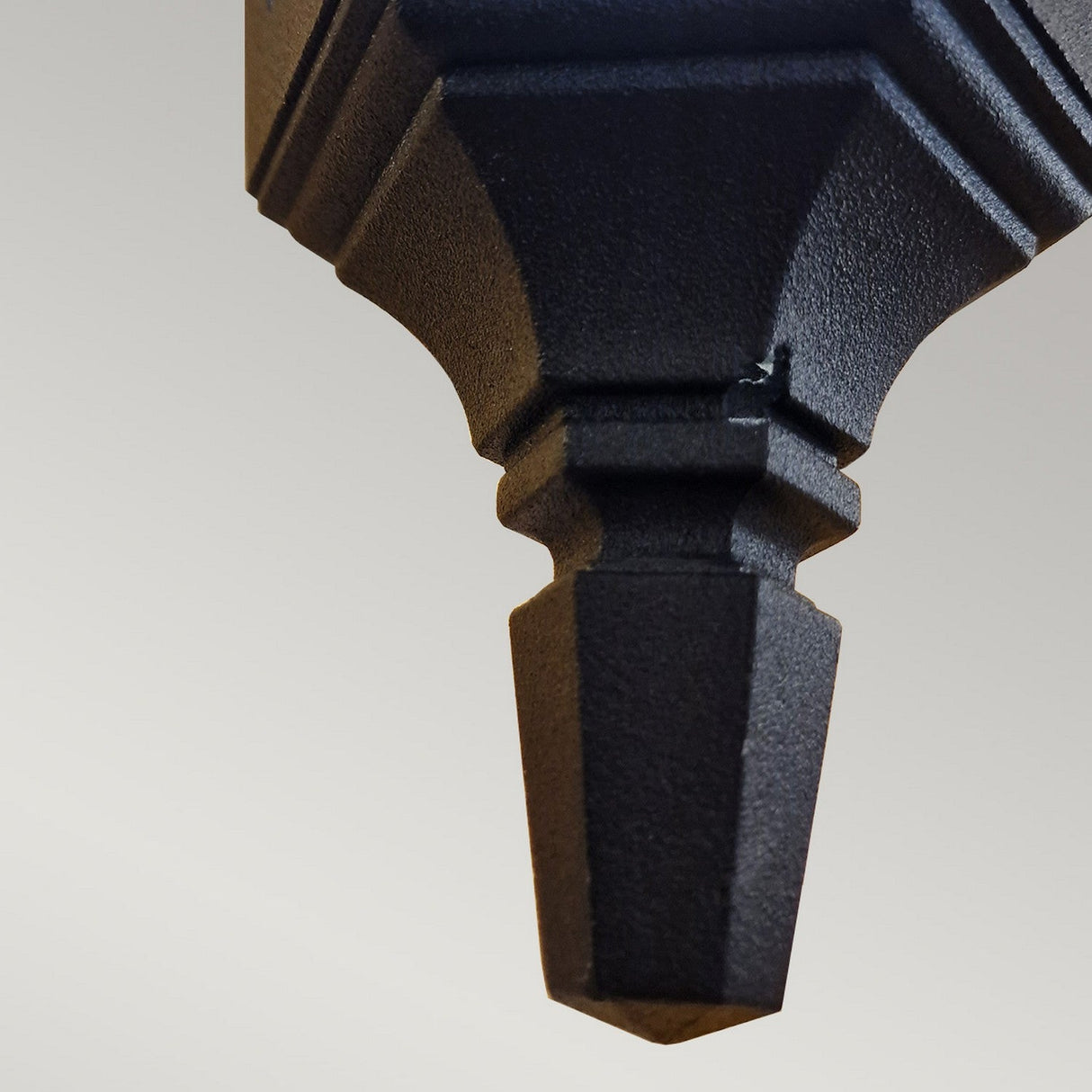 A close-up of the Parish Mini 1 Outdoor Light Down Wall Light in black, featuring an ornate geometric design against a light gray background. The textured surface accentuates the craftsmanship of this elegant piece.