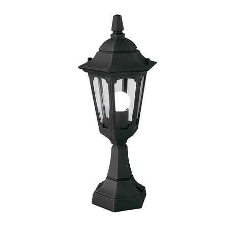 The Parish Mini 1 Light Pedestal Light in black features a vintage-style outdoor lantern design with a glass enclosure and visible bulb inside. Its hexagonal structure and pointed top enhance its charm in outdoor lighting, elegantly showcased against a white background.