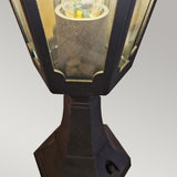 Detailed view of the Parish Mini 1 Light Pedestal Light in black featuring a hexagonal shape with clear glass panels, elegantly displaying an LED bulb inside. This sophisticated piece of outdoor lighting is set against a plain gray background, highlighting its timeless lantern design.