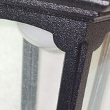 Close-up of the textured black metal frame of the Parish Mini 1 Light Outdoor Chain Pendant, featuring a black powder coating. The edge of its curved frosted glass lampshade can be seen, casting ambient lighting, with a blurred background.