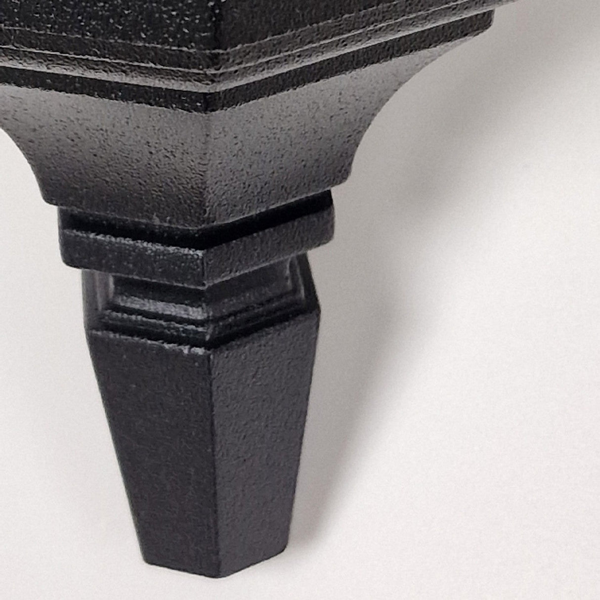 Close-up of a black, angular piece from the Parish Mini 1 Light Outdoor Chain Pendant against a white background. Its surface features a matte black powder coating with a geometric, tapered design that enhances its sleek appearance.