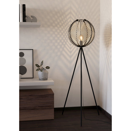 Prosena Floor Lamp in black and white, a tripod floor lamp with slim black steel legs and a round woven shade, shown lit in a living room corner.