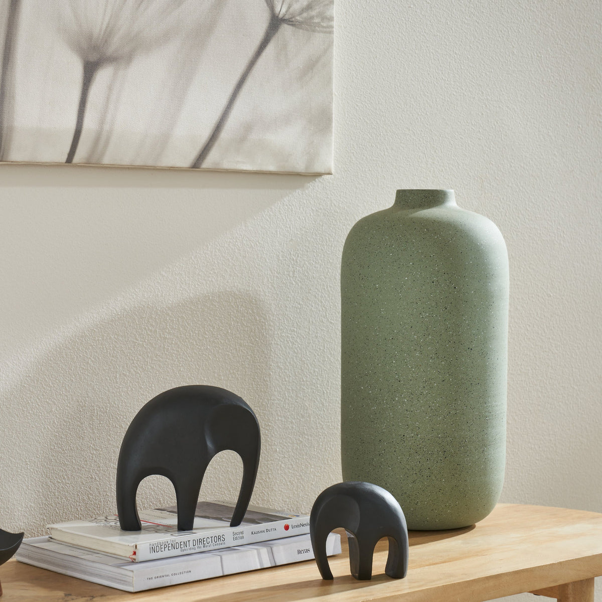Prush Metal Vase 40.5cm in sage green with fine speckled texture, tall bottle shape with narrow neck, styled on a wooden console table beside small black elephant figurines and stacked books.