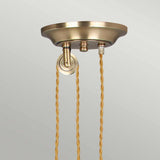 A detailed view of the Provence 1 Light Rise & Fall Pendant in aged brass, showcasing two gracefully twisting gold-colored cords descending from the vintage-inspired ceiling canopy. These cords are attached to the canopy through distinct fixtures, set against a simple light gray backdrop.