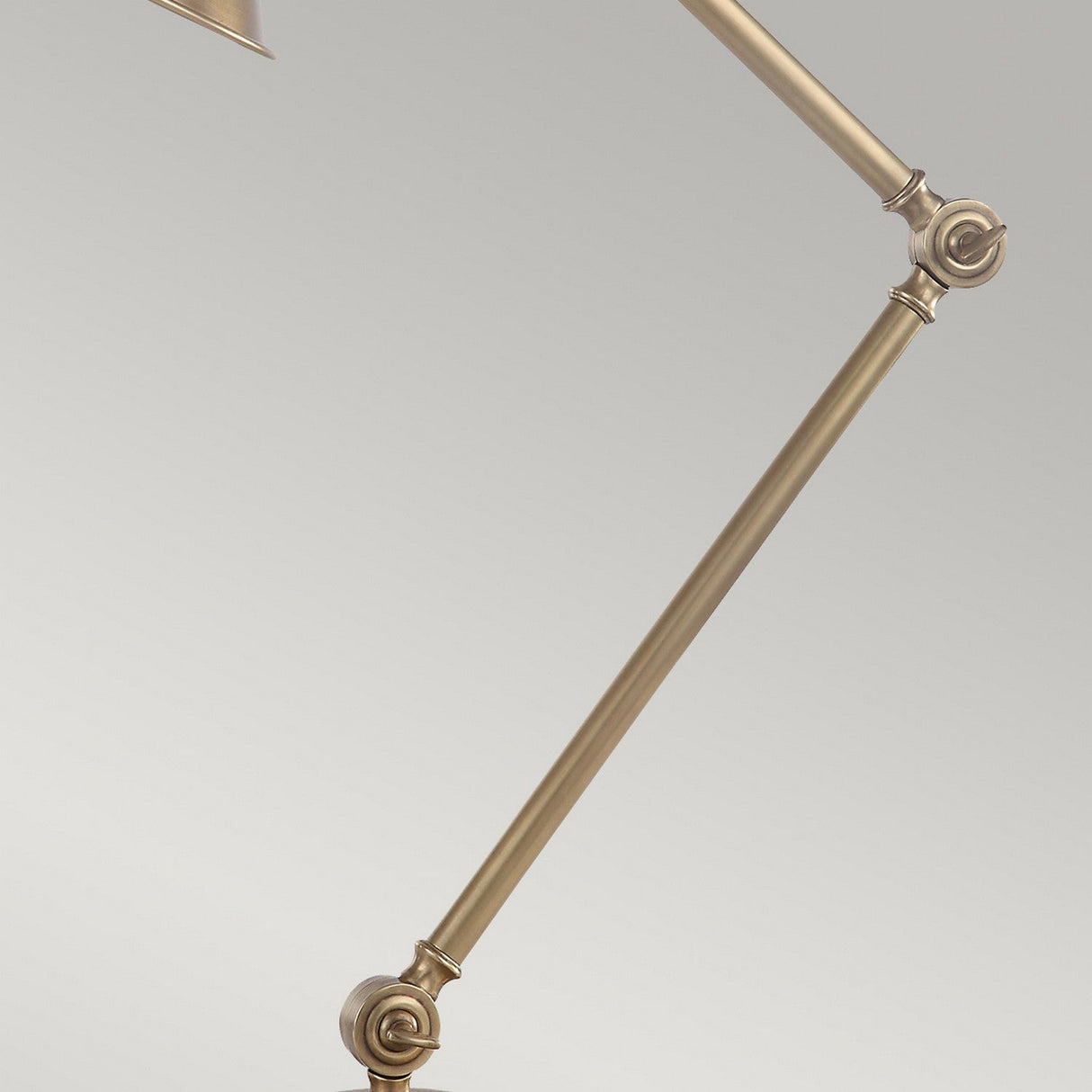 Close-up of the Provence 1 Light Table Lamp - Aged Brass with an adjustable brass arm, featuring visible joints and screws against a plain light gray background. The lamp is positioned diagonally across the image, accentuating its industrial design and aged brass finish.