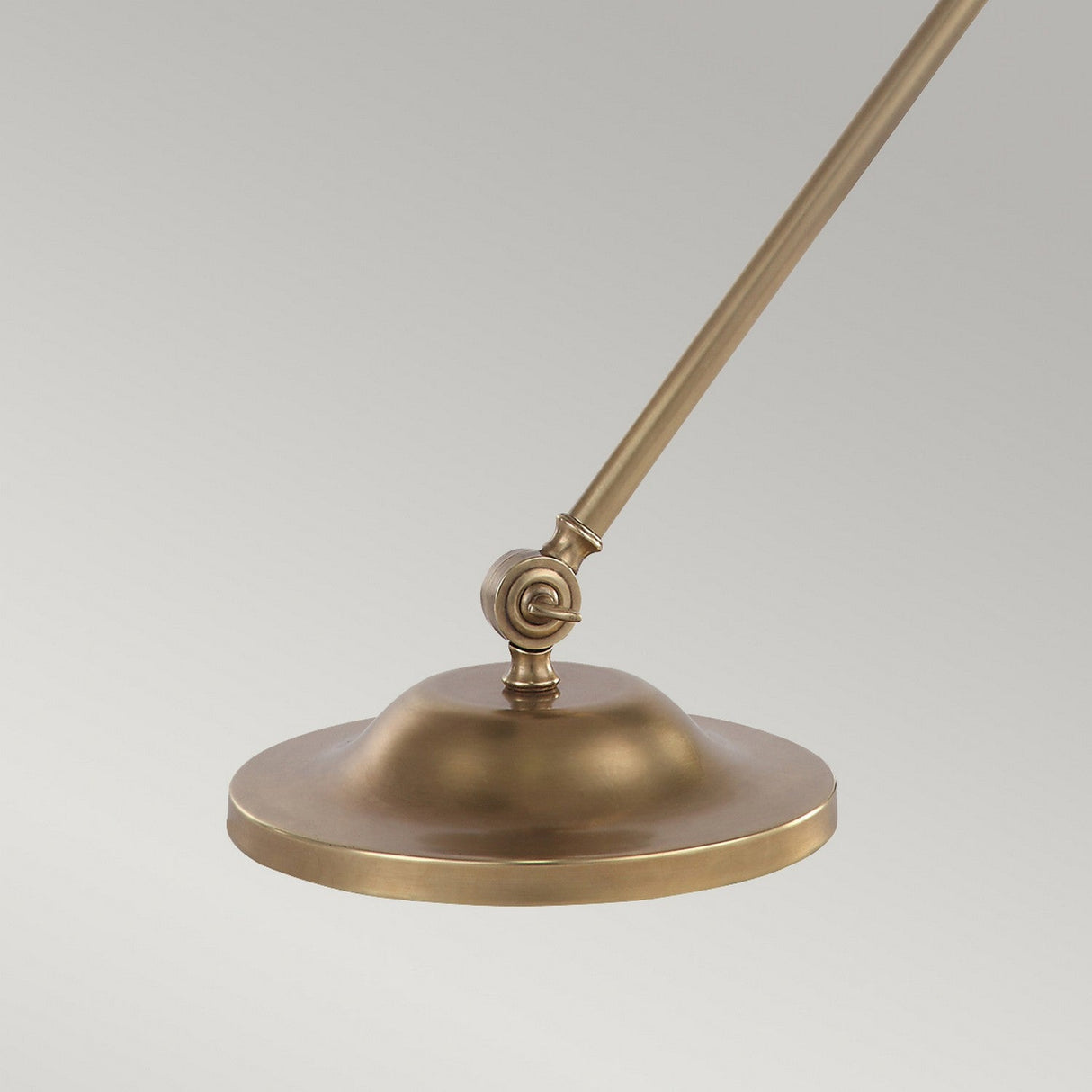 The Provence 1 Light Table Lamp - Aged Brass features a close-up view of its elegant design, showcasing a vintage charm with its round, flat shade on an adjustable arm. The shade has a sleek and simple appearance, and the joint allows for precise angle adjustments. Set against a plain light gray background, this lamp embodies timeless elegance and functionality.