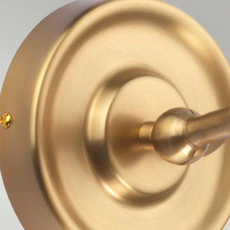 A close-up view of the Provence 1 Light Wall Light in aged brass reveals its vintage, metallic, gold-colored circular design with a central cylindrical extension. The fixture's smooth and polished surface elegantly reflects light, enhancing its presence. Mounted on a light gray wall, this wall light brings timeless charm to the space.