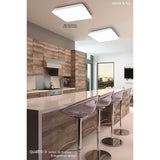 Two Mantra Quatro II square LED flush ceiling lights in matt white acrylic with chamfered corners, installed above a modern wood kitchen island with bar stools.