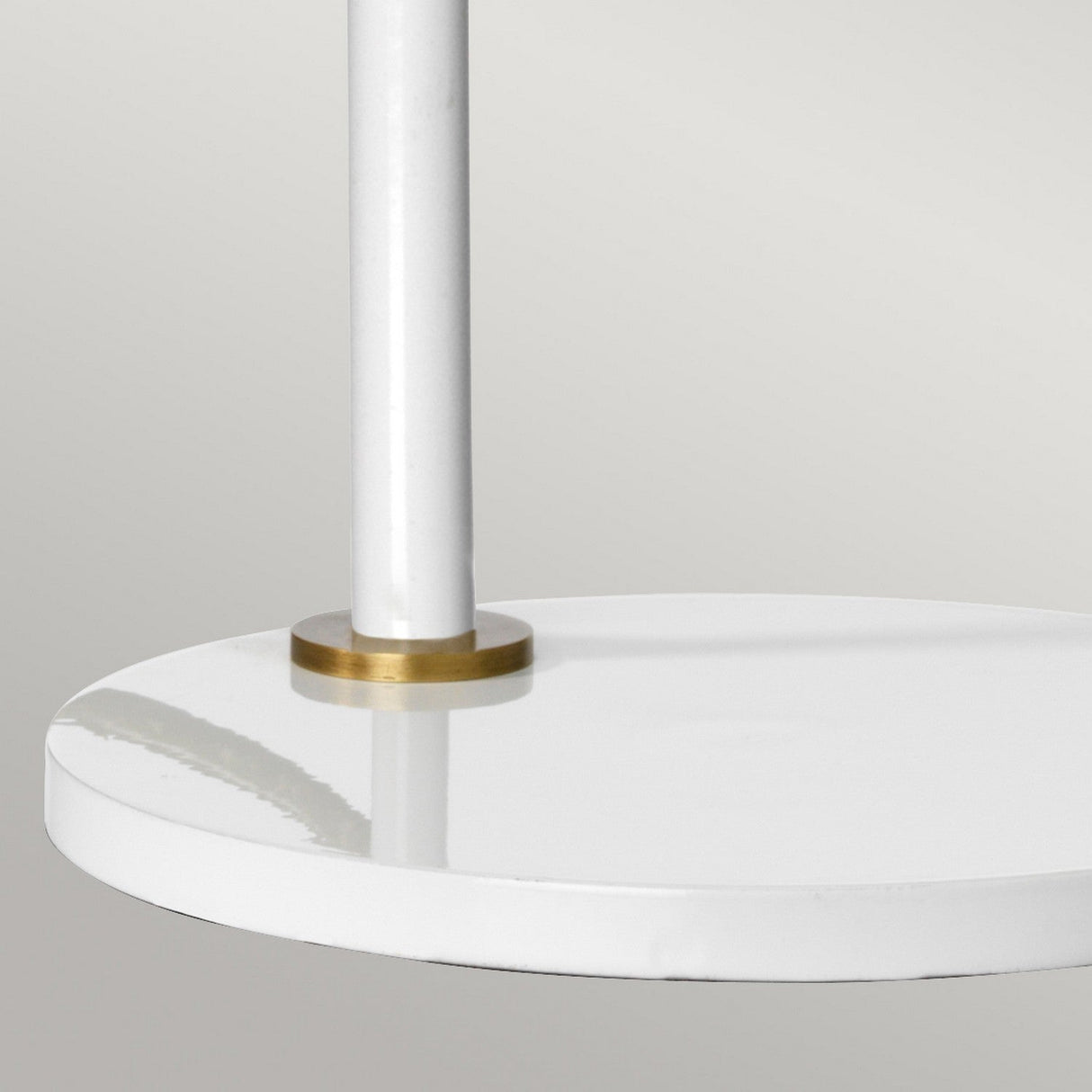 Close-up of the Quinto 1 Light Table Lamp - White/Aged Brass featuring a sleek, round white base with a minimalist design. A subtle aged brass accent elegantly divides the base and pole, set against a light gray background.